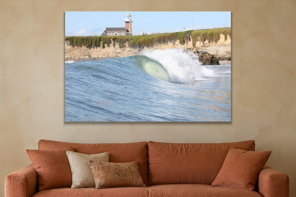 A glassy wave breaking along a cliff below a brick lighthouse shown large on the wall of a lived-in room
