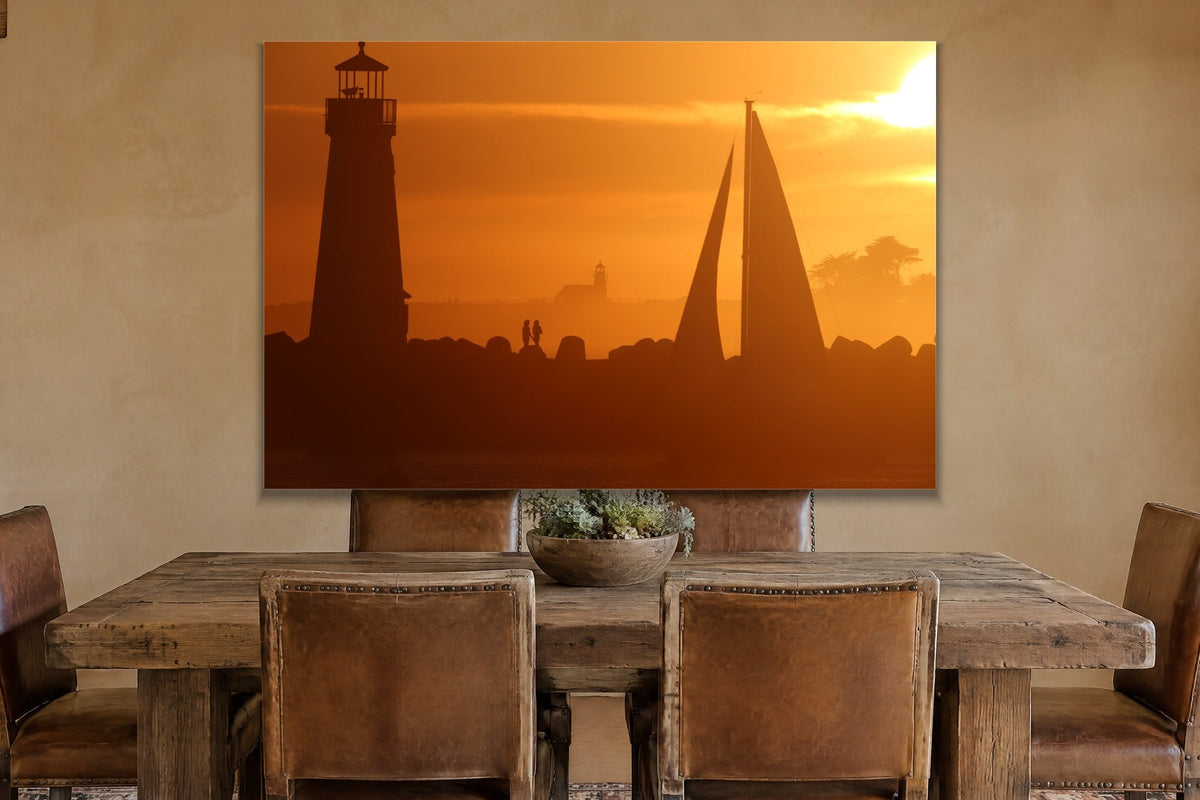 A lighthouse and a sailboat sail in silhouette against an orange sunset shown large on the wall of a lived-in room