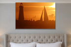 A lighthouse and a sailboat sail in silhouette against an orange sunset shown large on the wall of a lived-in room
