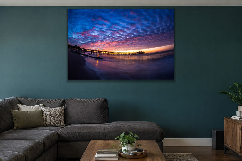 A fisheye view of a long pier under a sky of blue and pink clouds at sunset shown large on the wall of a lived-in room