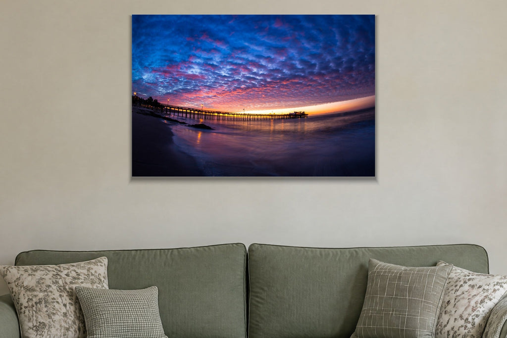 A fisheye view of a long pier under a sky of blue and pink clouds at sunset shown large on the wall of a lived-in room