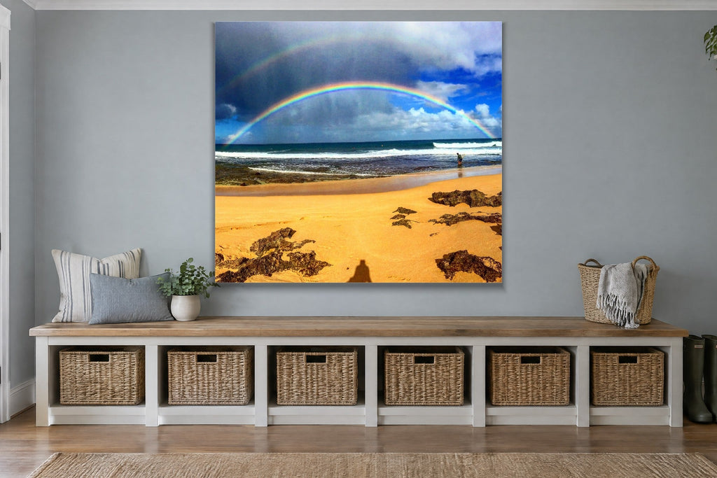 A rainbow over a gold sand beach with a lone person at the waterline shown large on the wall of a lived-in room