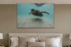 A sea turtle swimming over sand in clear turquoise water shown large on the wall of a lived-in room