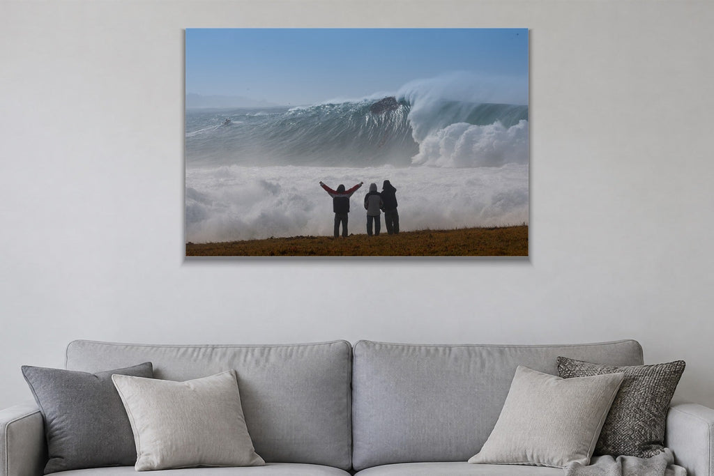 Three people with arms raised on a bluff facing an enormous wave and cloud of spray shown large on the wall of a lived-in room
