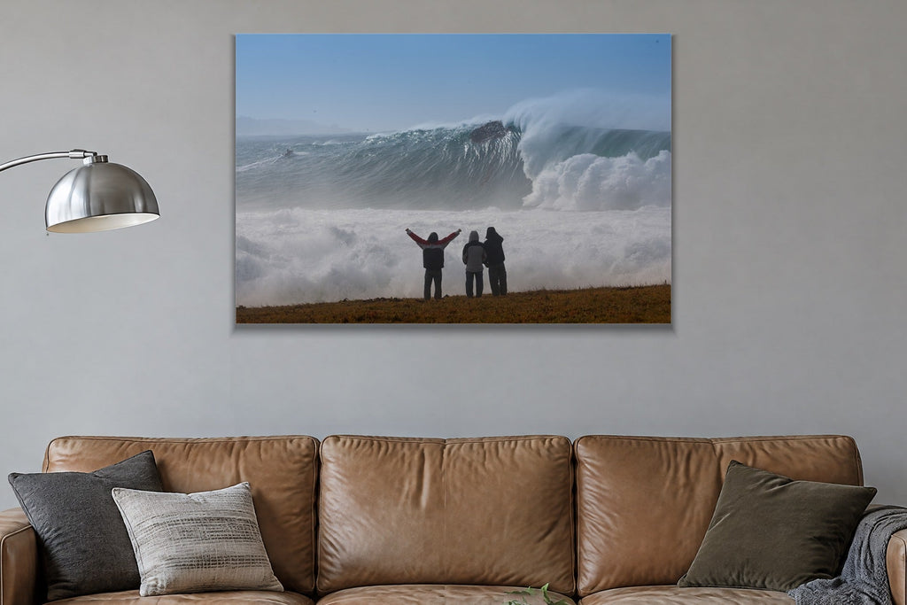 Three people with arms raised on a bluff facing an enormous wave and cloud of spray shown large on the wall of a lived-in room