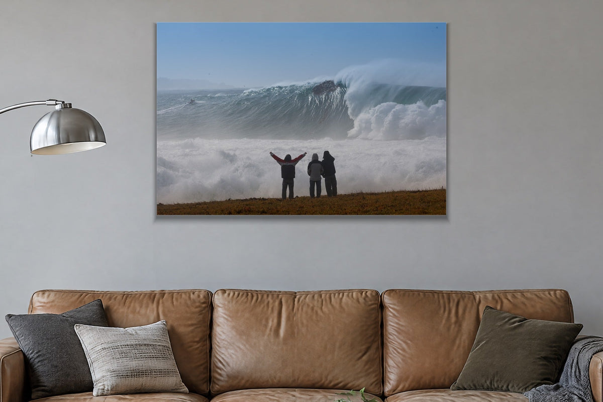 Three people with arms raised on a bluff facing an enormous wave and cloud of spray shown large on the wall of a lived-in room