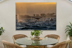 A whale fluke rising above dark water at golden hour with a second whale beside it shown large on the wall of a lived-in room