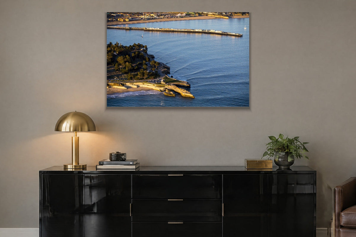 An aerial view of a long wharf and rocky point in blue water at golden hour shown large on the wall of a lived-in room