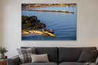 An aerial view of a long wharf and rocky point in blue water at golden hour shown large on the wall of a lived-in room