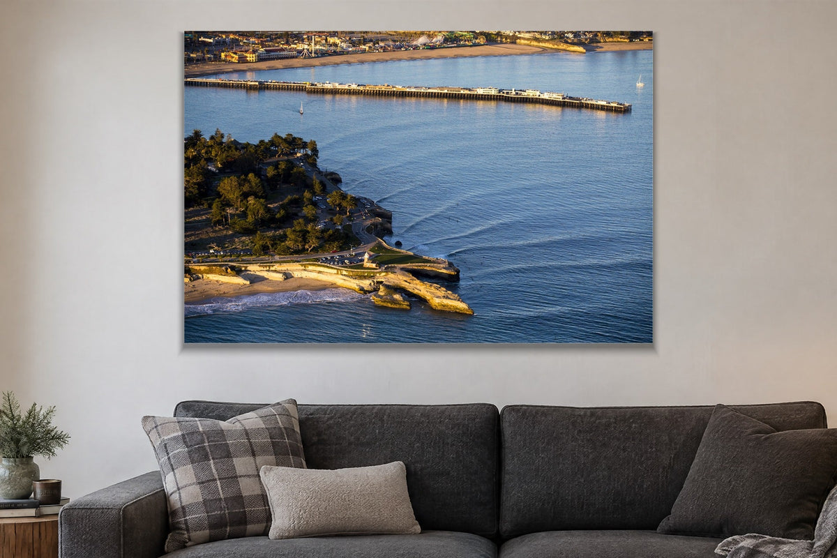 An aerial view of a long wharf and rocky point in blue water at golden hour shown large on the wall of a lived-in room